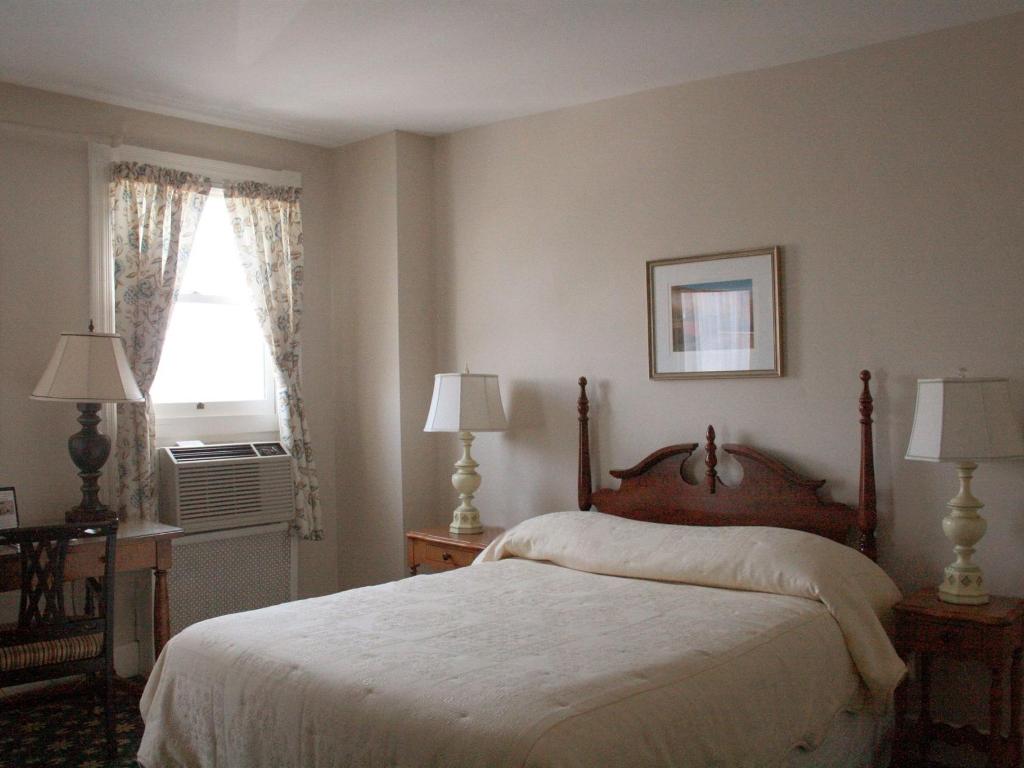 A bedroom with floral curtains and large bed with white bedding and wooden frame sit in the middle of the room. Antique lamps sit on either side of the bed.